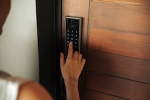 A hand presses a numeric keypad mounted in a door frame; purple-tinted image with a wooden door panel visible on the right.