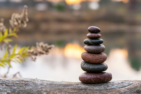 A tall stack of smooth stones balanced on a pebbled beach, with the sea and a distant horizon under a purple-tinted sky.