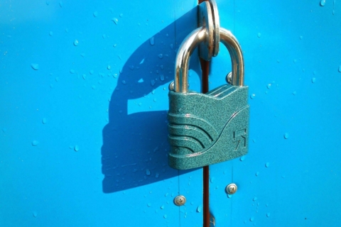 Shiny metal padlock on a purple door, covered with water droplets, casting a dark shadow to the left.