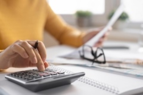Calculator resting on scattered receipts and documents on a desk, with a laptop in the background and a stack of cash nearby.