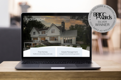 Open laptop on a wooden table displaying a real estate website with a large house image, navigation bar, two service cards, and an award badge.