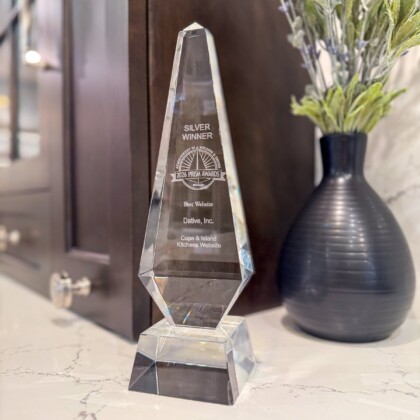 Crystal award trophy engraved with Silver Winner 2024 Prism Awards for Best Website by Dative, Inc. Cape & Island Kitchens Website, displayed on a marble countertop next to a black vase with dried lavender sprigs